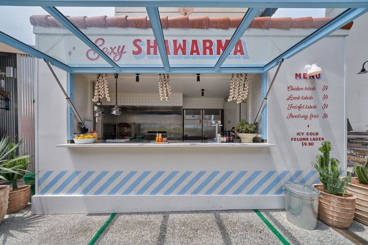 an outdoor restaurant with blue and white stripes on the outside wall, along with potted plants