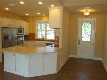 an empty kitchen with wood floors and white cabinets is pictured in this image, there are lights on above the island