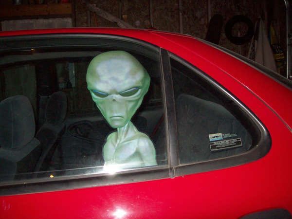 an alien head sitting in the passenger seat of a red car