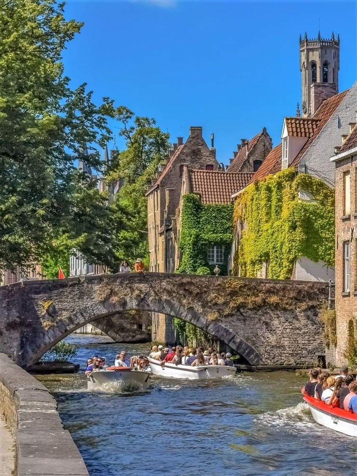 people are riding in boats on the water near buildings and a stone bridge over a river