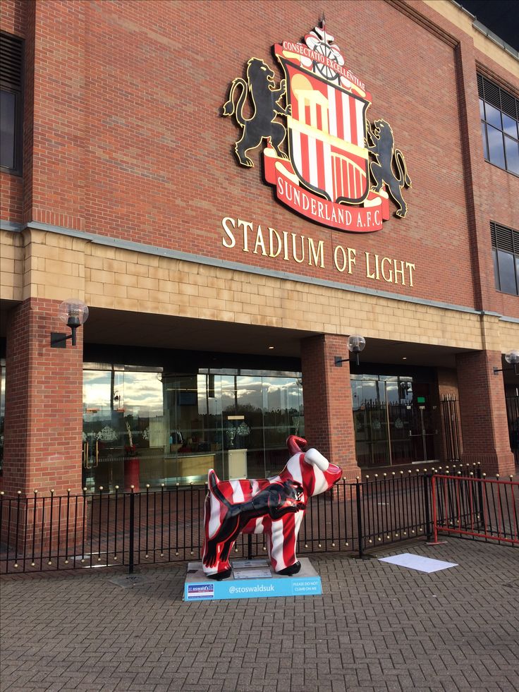 a large red and white dog statue sitting in front of a stadium with the words stadium of light on it