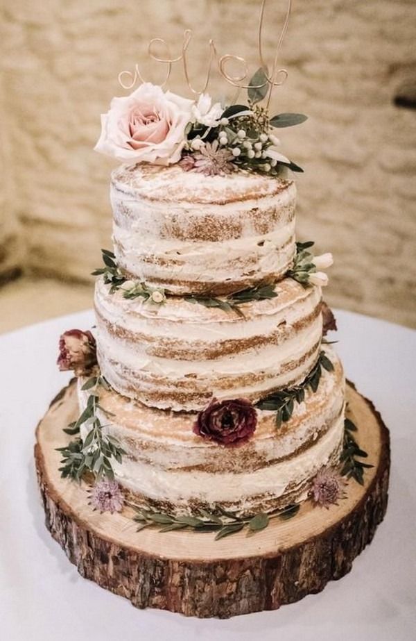 a three tiered wedding cake with flowers and leaves on top is sitting on a wooden slice