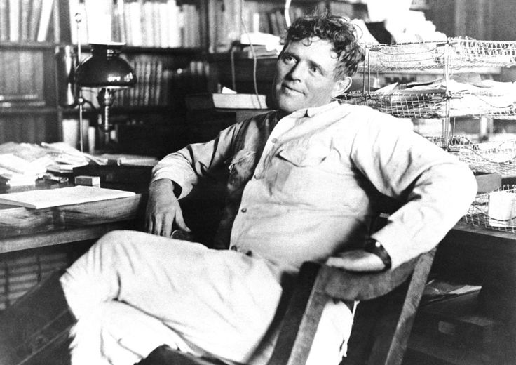 black and white photograph of a man sitting at a desk in front of bookshelves