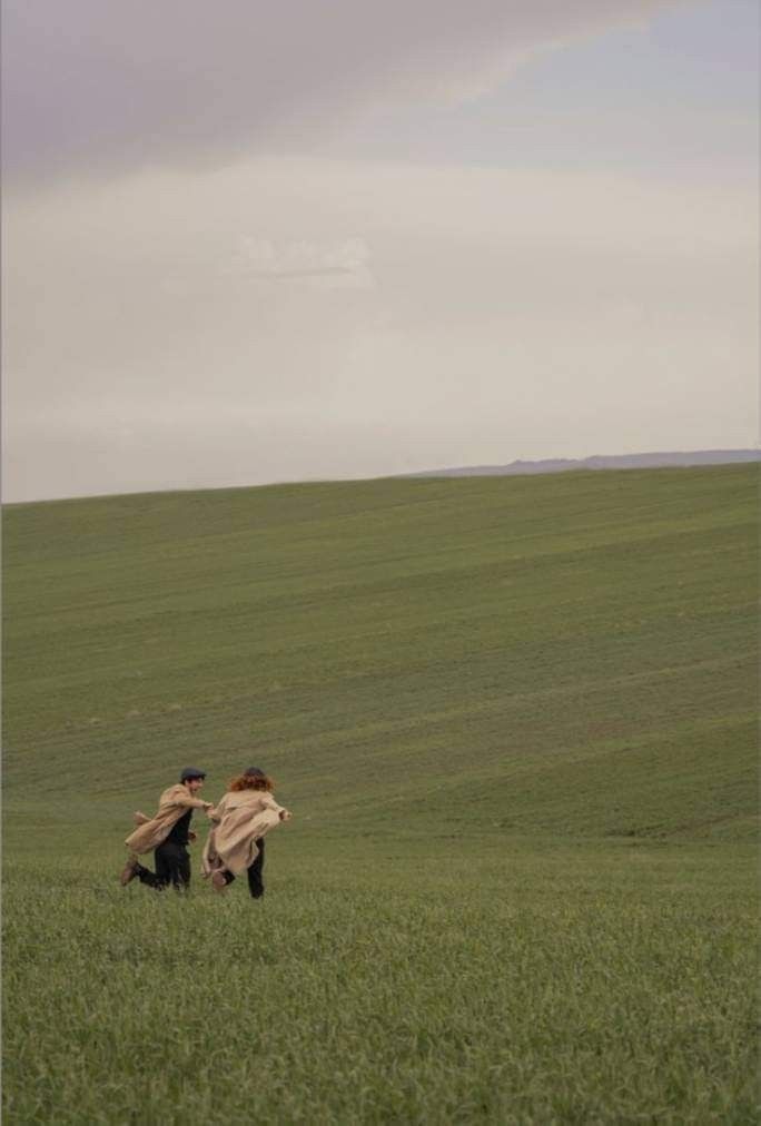 two people running in the grass with a kite