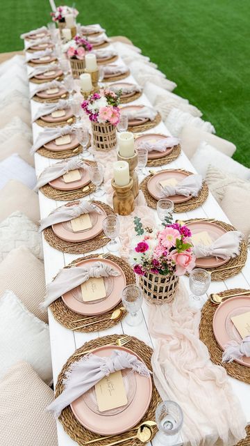 a long table set with pink and white plates, place settings and flowers on it