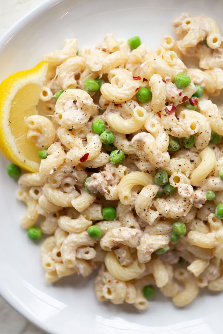 a white plate topped with macaroni and peas next to a slice of lemon