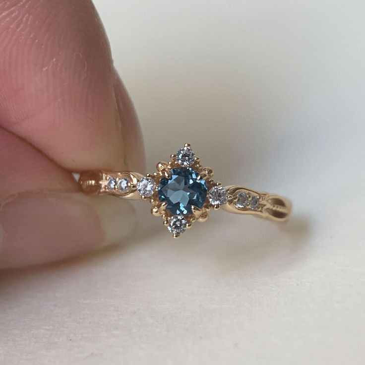 a person holding a ring with a blue stone in it's center and diamond accents around the band