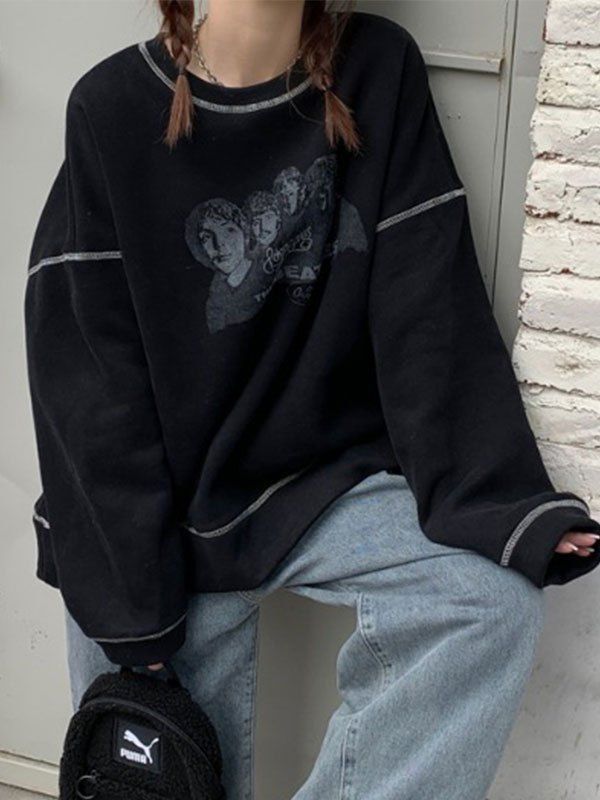 a woman sitting on the side of a building wearing a black sweater and hat with her hands in her pockets