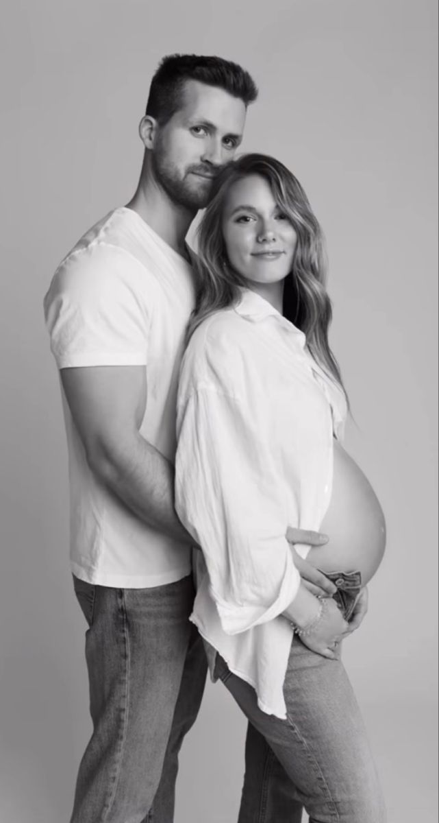 a man and woman pose for a black and white photo while holding their pregnant belly