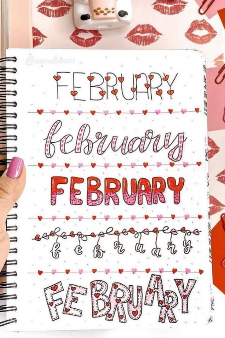 a hand holding a notebook with the words february written in red and pink on it