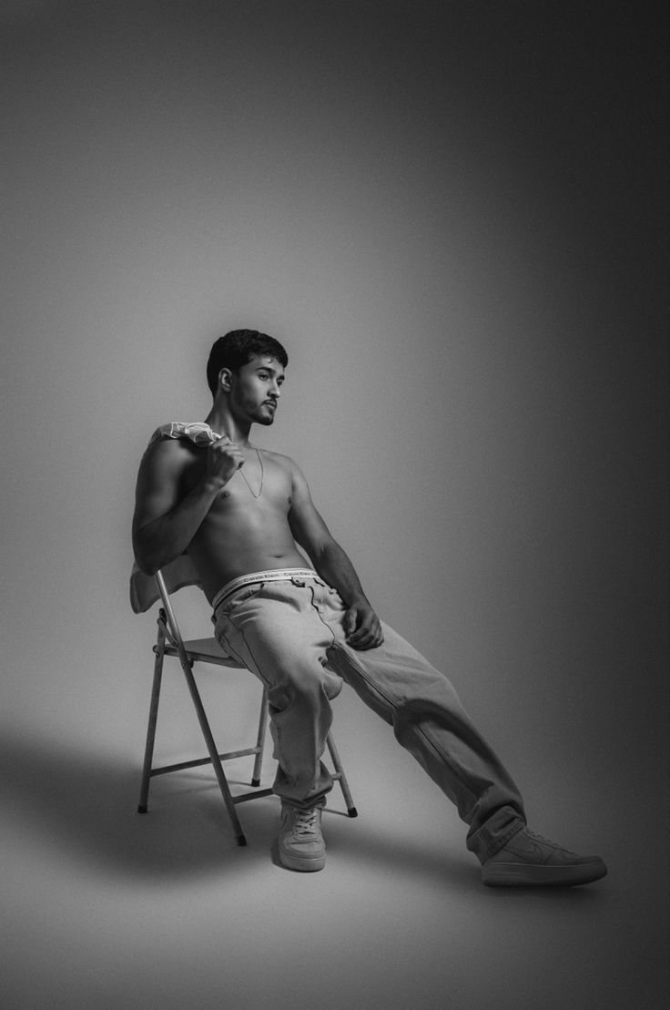 a man sitting on top of a chair in front of a white wall with his legs crossed