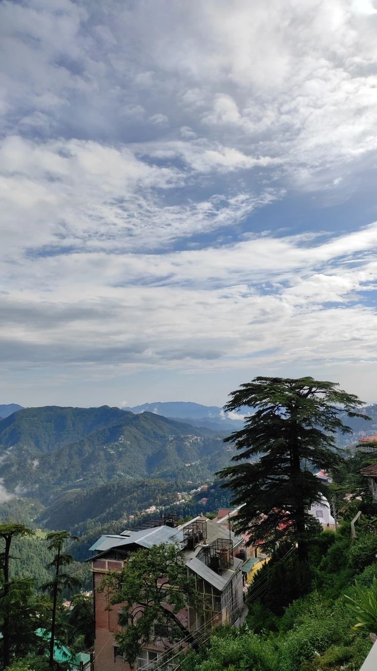 a scenic view of mountains and trees from the top of a hill with clouds in the sky