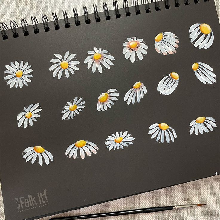 a black notebook with white and yellow daisies on it next to a pair of scissors