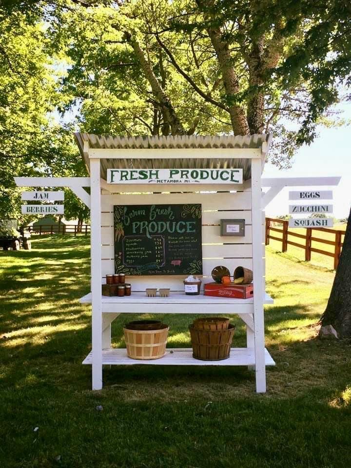 a sign for fresh produce on display in the grass with trees and signs behind it