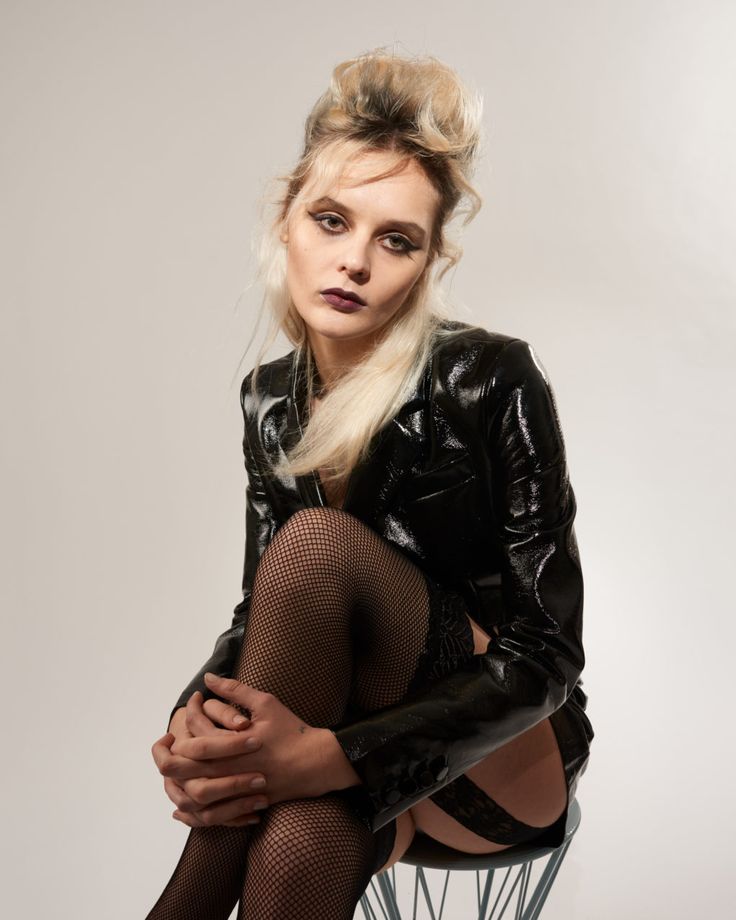 a woman in fishnet stockings and black leather jacket sitting on a chair with her legs crossed