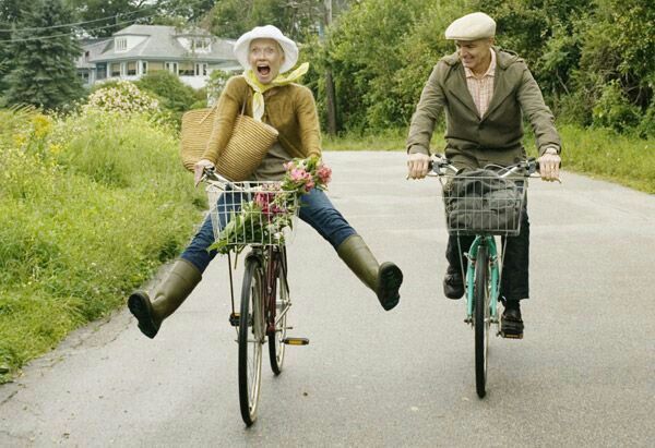 two people riding bikes down a road with an old woman on the front and man on the back