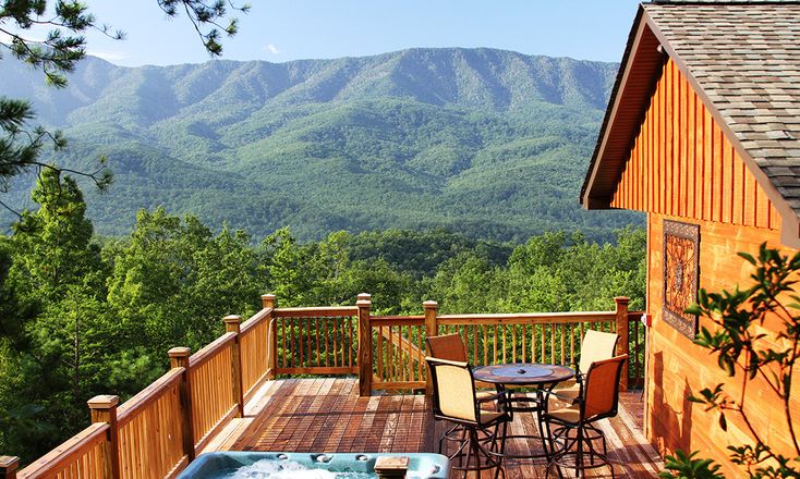 a hot tub sitting on top of a wooden deck next to a building with mountains in the background