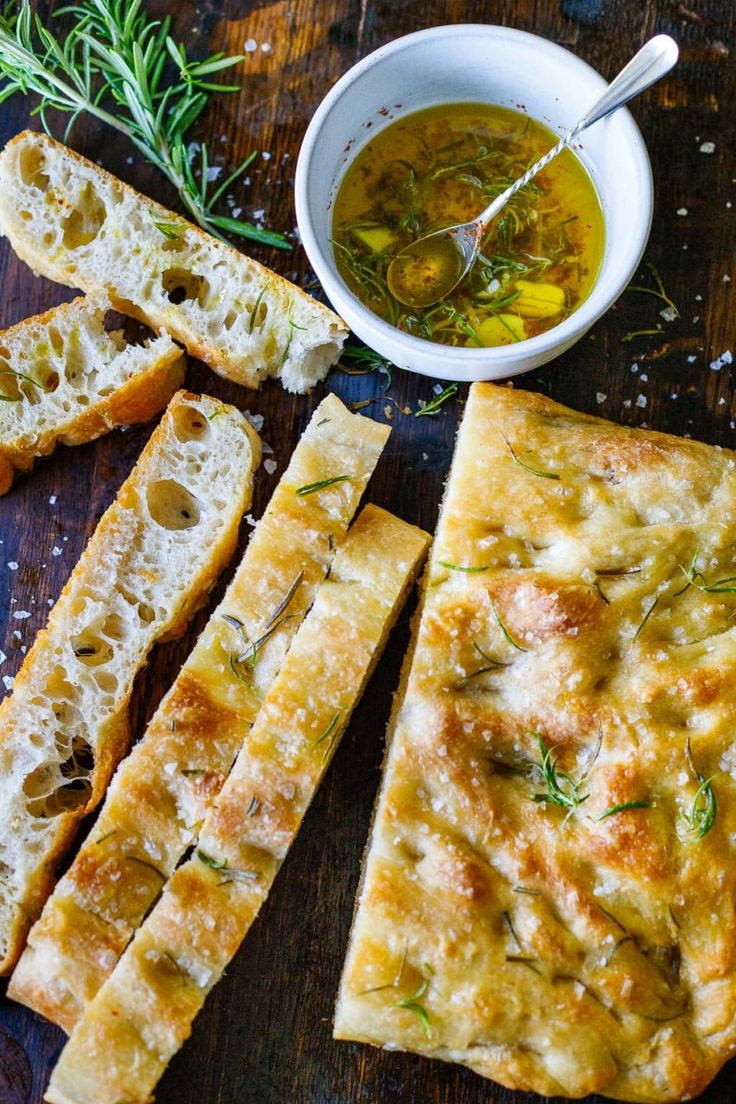 bread sticks with olive oil and rosemary sprigs next to them on a wooden table