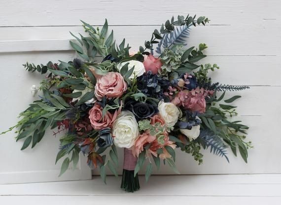 a bridal bouquet is displayed against a white painted wood paneled wall with greenery and foliage