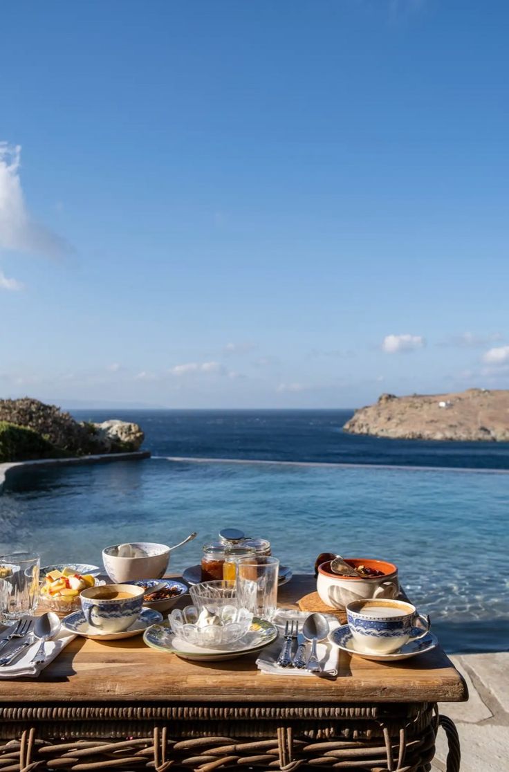 an outdoor table with food and drinks on it near the water's edge,