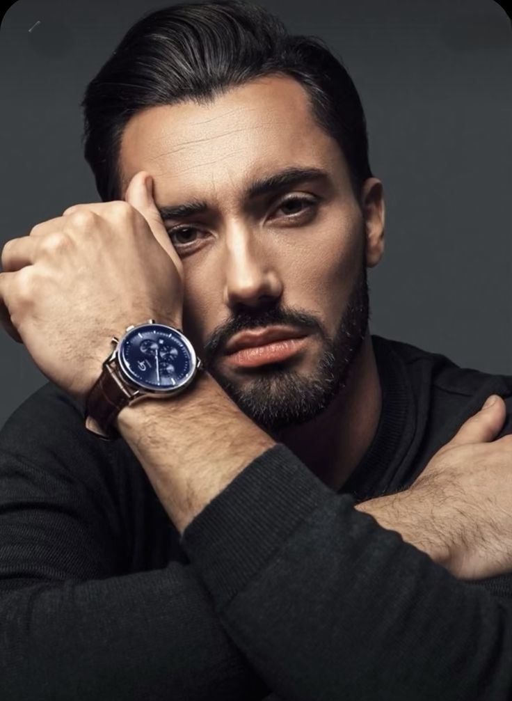 a man with a watch on his wrist is posing for a photo in front of a gray background