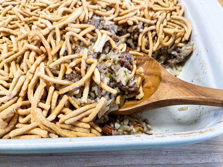 a casserole dish filled with lots of food and a wooden spoon in it