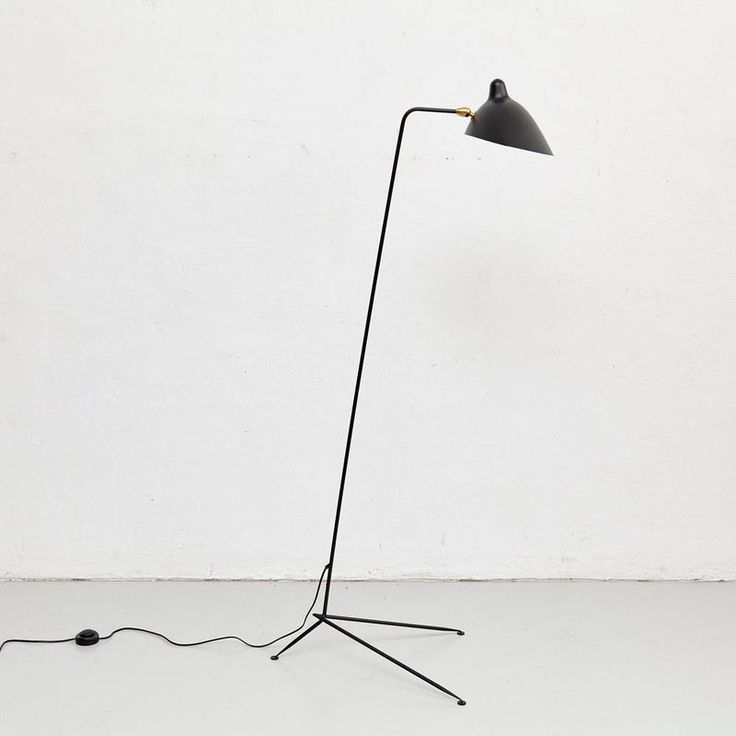 a black floor lamp with a white wall behind it and a wire on the ground