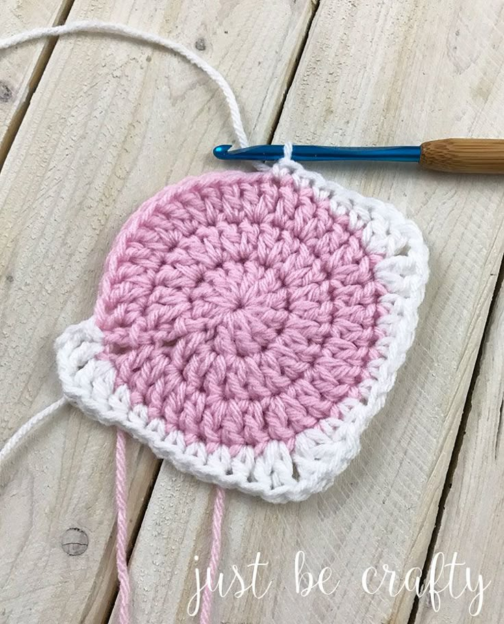 a crocheted pink and white potholder with a blue handle on a wooden surface