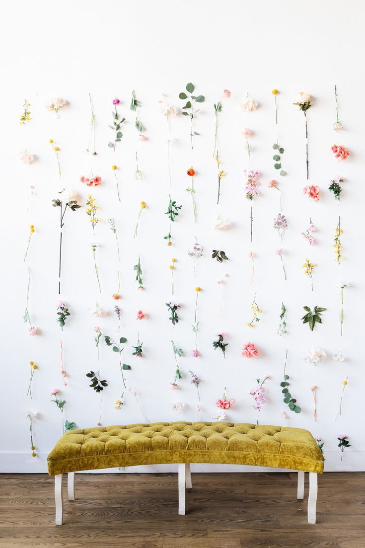 a yellow bench sitting in front of a wall with flowers hanging on it's sides