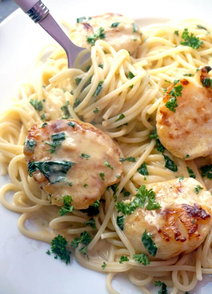 a white plate topped with pasta and meat covered in sauce, garnished with parsley