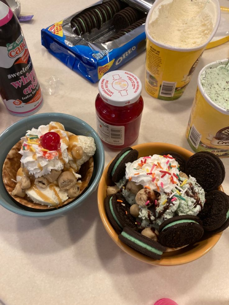 two bowls filled with ice cream and cookies on top of a table next to drinks