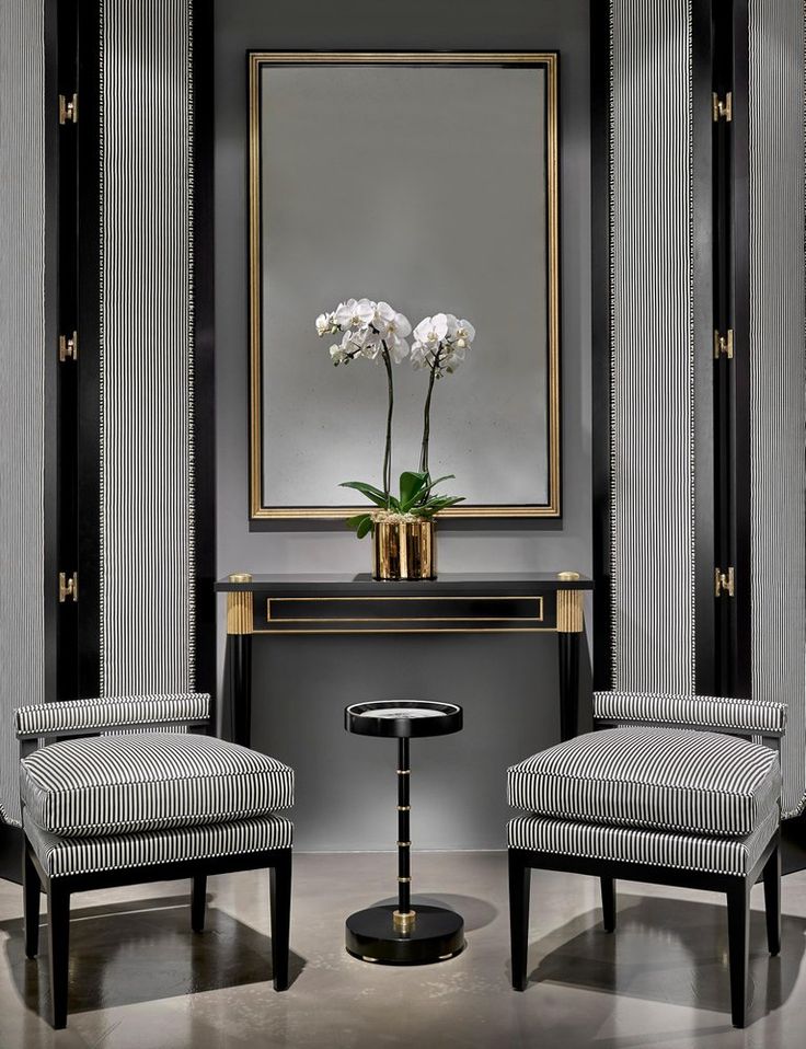 two chairs and a table in front of a large mirror with flowers on the table