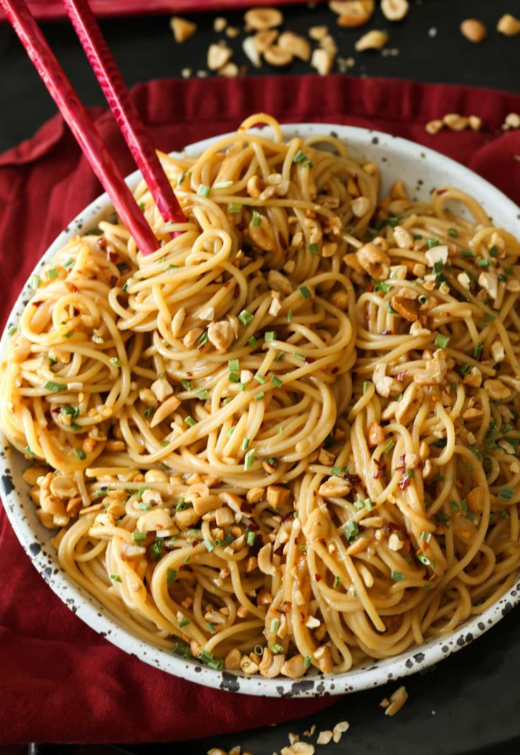 a bowl full of noodles with chopsticks in it and peanuts on the side