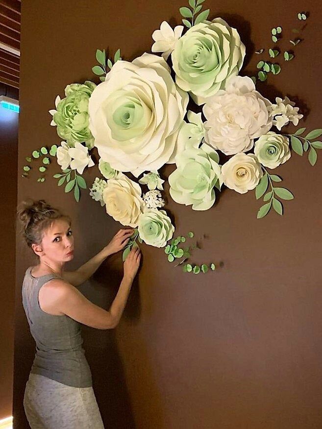 a woman standing next to a wall with paper flowers on it