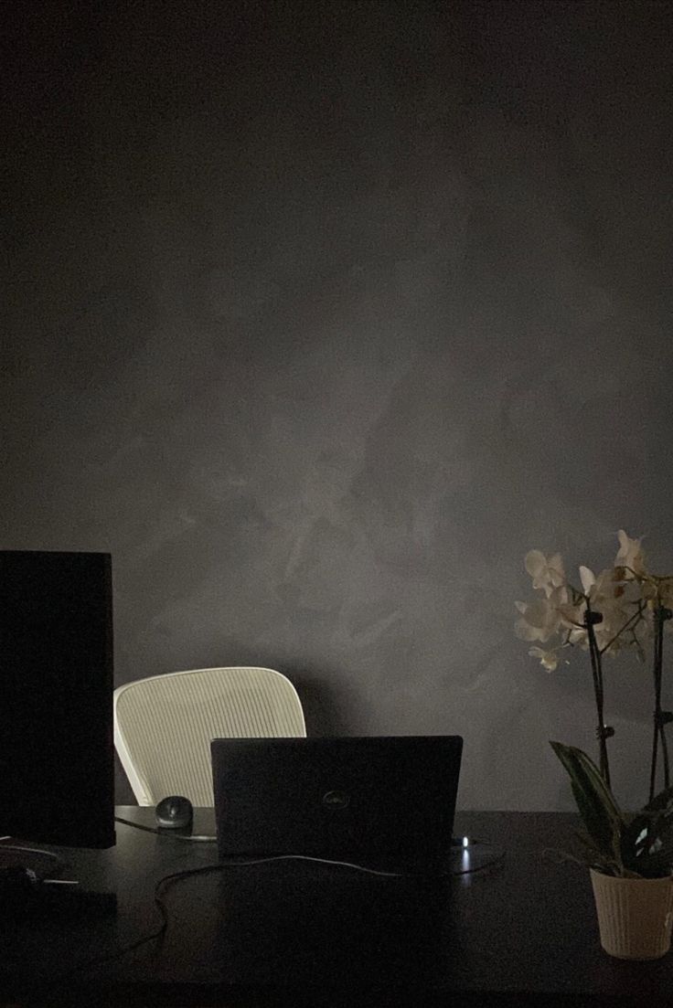 a laptop computer sitting on top of a wooden desk next to a vase with flowers