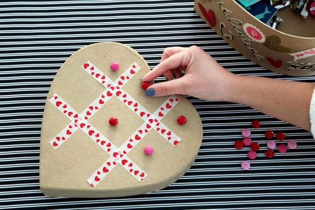 a person making a heart shaped craft with candy on the table next to some other items