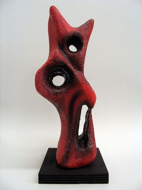 a red and black sculpture is on a black stand against a white background that has the shape of a cat's head