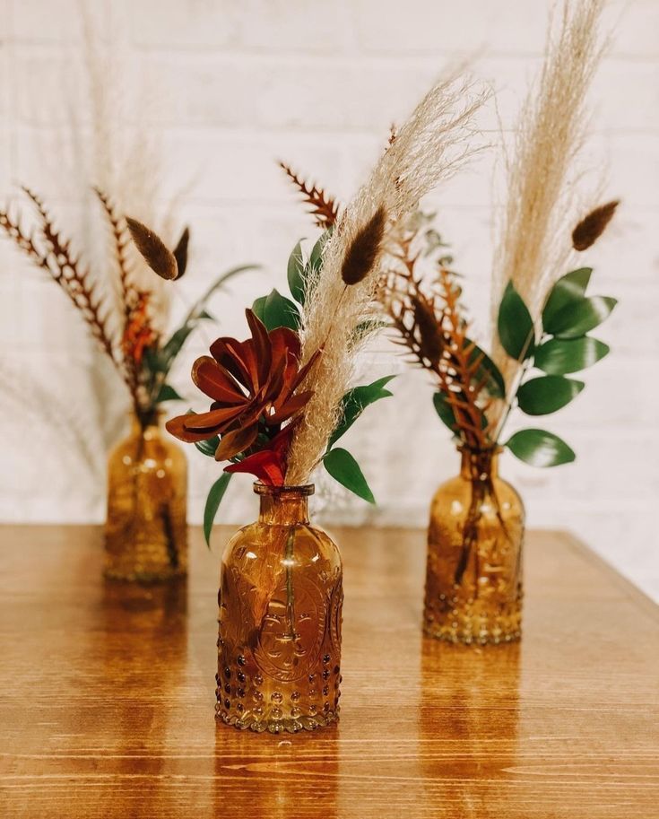 three glass vases with flowers and plants in them