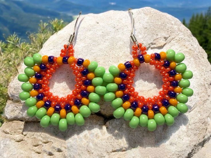 Add a splash of color to your accessories with these vibrant handmade seed bead earrings from Lakefront Jewels by Gina. Crafted with a delightful mix of lime green, orange, yellow, and shiny purple seed beads, these earrings are designed to brighten up any outfit. Featuring a comfortable French ear wire hook, these earrings are as fun as they are stylish. Details: Adjustable: N/A Finding Color: Silver Focal Point: Bright and colorful seed beads Other Beads Include: N/A Handmade: Yes Unique Gift: Perfect for someone who loves vibrant jewelry One of a Kind: Absolutely Good For: Adding a fun pop of color to any outfit Ready to Ship: This one-of-a-kind item is completed and ready to ship. Stone Meaning: Seed beads are known for their versatility and ability to create intricate patterns. The br Green Beaded Earrings For Summer, Vibrant Handmade Beaded Earrings For Summer, Green Beaded Earrings For Crafting In Summer, Vibrant Beaded Earrings As A Gift, Vibrant Beaded Earrings For Gifts, Green Beaded Earrings With Large Beads For Gift, Summer Green Earrings With Tiny Beads, Green Earrings With Colorful Beads, Vibrant Handmade Beaded Earrings For Beach