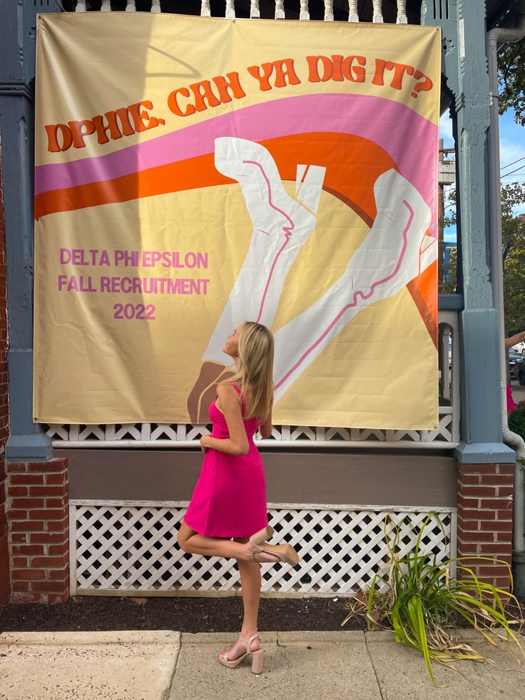 a woman in a pink dress standing next to a large poster on the side of a building