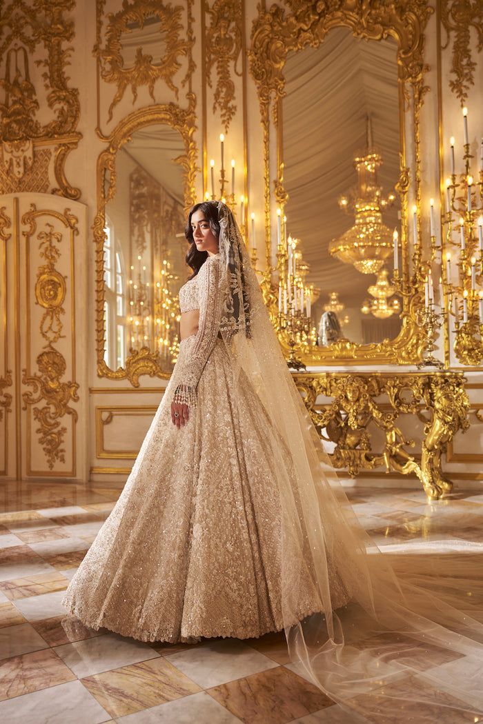 a woman in a wedding dress standing next to a gold chandelier and mirror