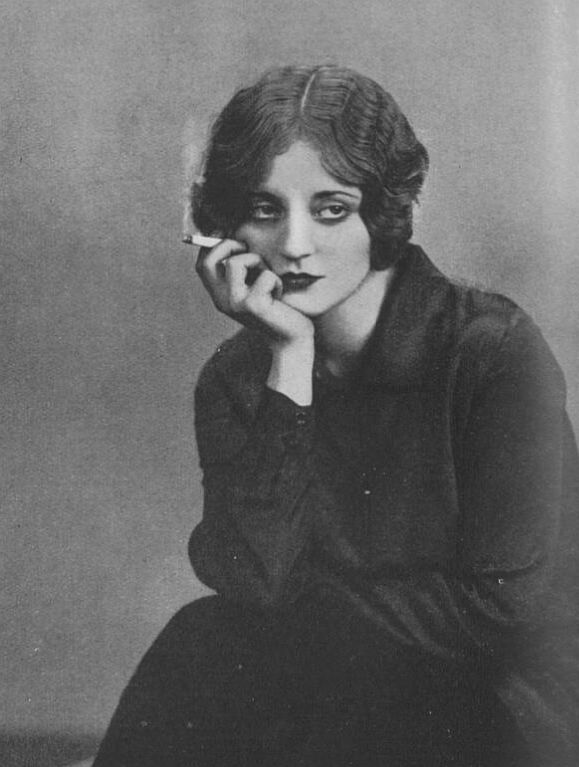 an old black and white photo of a woman with her hand on her chin sitting down