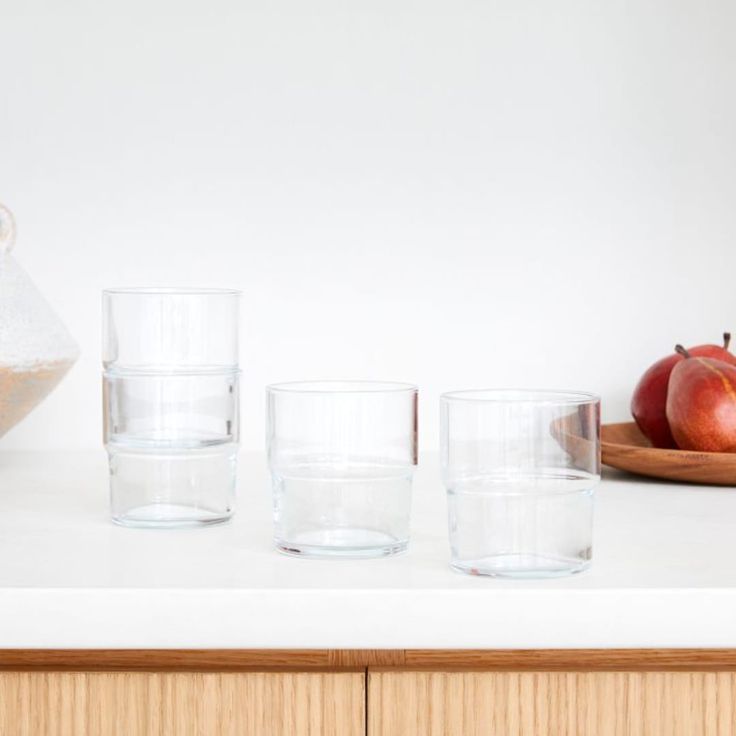 three glasses are lined up on a counter with apples in the background and an apple bowl next to them