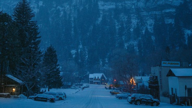 cars parked on the side of a snow covered road in front of a snowy mountain