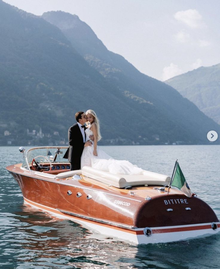 a bride and groom are kissing on the back of a boat in the water with mountains in the background