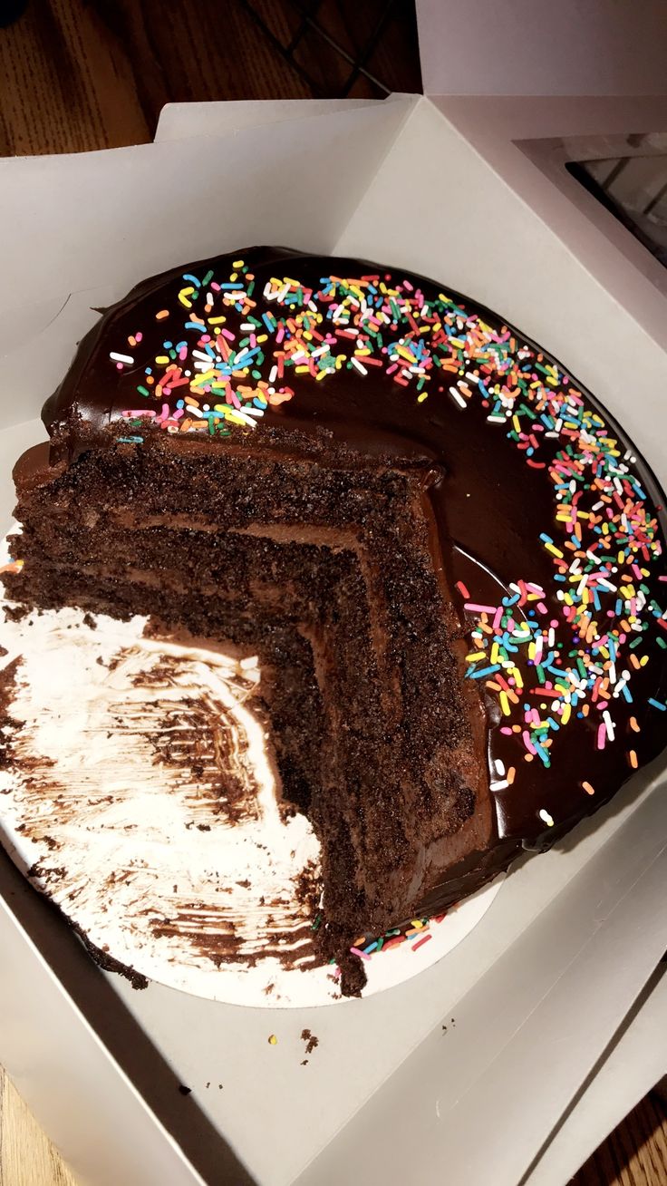 a chocolate cake with frosting and sprinkles in a box on a table