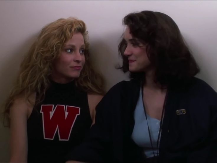 two women sitting next to each other in front of a white wall with the letter w on it