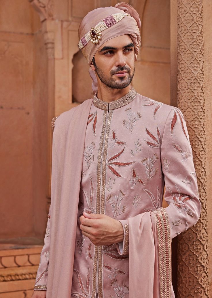 Step into the spotlight with the stunning Nude Pink Embroidered Sherwani Set, a creation that embodies grace and grandeur. Made from luxurious silk jacquard, the pink sherwani is adorned with intricate tonal velvet applique work and floral butta motifs, highlighted with zari and dabka embroidery, adding a touch of opulence. Paired with a matching kurta and pants, designed for a comfortable yet stylish fit, and completed with an embroidered stole, this ensemble ensures both a rich texture and a refined appearance. Ideal for the groom on his special day, this outfit combines traditional craftsmanship with contemporary design, offering a timeless appeal that exudes elegance. Composition : Sherwani, Stole, Kurta and Churidar - Silk JacquardCare: Dry Clean Only and Vacuum Storage Delivery : 4-6 Pink Resham Embroidered Bandhgala For Formal Occasions, Formal Pink Bandhgala With Resham Embroidery, Pink Sherwani With Chikankari Embroidery For Reception, Pink Embroidered Bandhgala With Traditional Drape, Embroidered Pink Bandhgala With Traditional Drape, Traditional Pink Long Sleeve Bandhgala, Traditional Long Sleeve Pink Bandhgala, Pink Bandhgala With Zari Work And Long Sleeves, Pink Raw Silk Sherwani With Traditional Drape