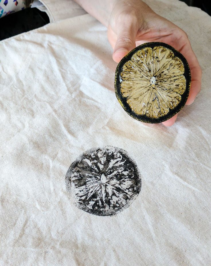 a person holding an object in their hand on top of a white cloth with black and yellow designs