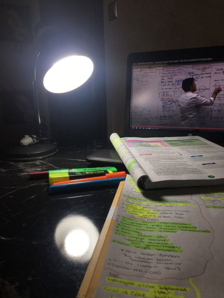 an open book sitting on top of a desk next to a laptop computer and light